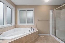 Soaking tub with tiled surround, dual windows with frosted glass, and an adjacent glass-enclosed shower - 