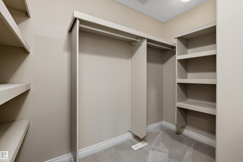 Walk-in closet featuring built-in shelving, hanging rods, neutral wall color, white baseboards, and patterned carpet flooring - 11203 72 Avenue Nw, Edmonton, AB - Indoor With Storage