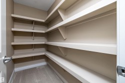 Walk-in pantry featuring light-toned walls, multiple levels of white shelving, patterned flooring, and white baseboards - 