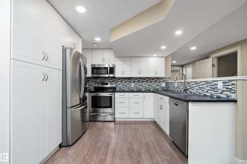 Modern kitchen featuring white shaker cabinetry, stainless steel appliances, dark countertops, a mosaic tile backsplash, and wood-finish flooring - 11203 72 Avenue Nw, Edmonton, AB - Indoor Photo Showing Kitchen With Upgraded Kitchen