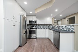 Modern kitchen featuring white shaker cabinetry, stainless steel appliances, dark countertops, a mosaic tile backsplash, and wood-finish flooring - 