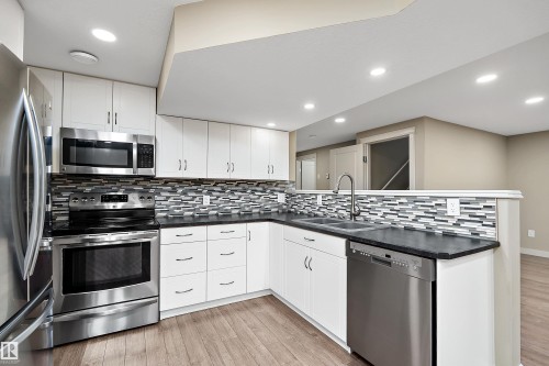 Modern kitchen featuring stainless steel appliances, white cabinetry, dark countertops, a mosaic tile backsplash, and wood-finish flooring - 11203 72 Avenue Nw, Edmonton, AB - Indoor Photo Showing Kitchen With Double Sink With Upgraded Kitchen