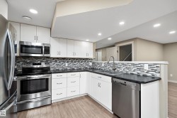 Modern kitchen featuring stainless steel appliances, white cabinetry, dark countertops, a mosaic tile backsplash, and wood-finish flooring - 