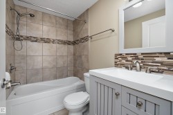 Bathroom featuring a white bathtub, tiled shower surround with decorative accent band, and a vanity with a white countertop - 