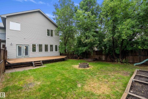 Expansive backyard featuring a large wooden deck with steps, a stone fire pit, wood fencing, and mature trees - 11203 72 Avenue Nw, Edmonton, AB - Outdoor With Backyard