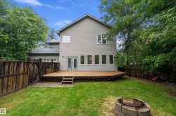 Expansive backyard featuring a large wooden deck with steps to the lawn, a stone fire pit, and mature perimeter trees - 