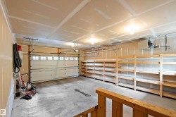 Spacious garage featuring a concrete floor, built-in wooden shelving units, and an overhead garage door with windows - 