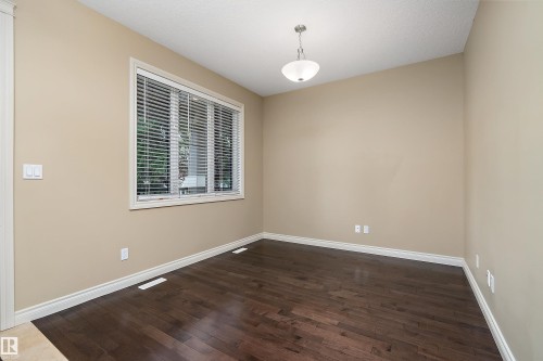 Spacious room featuring wood-finish flooring, neutral wall tones, white trim, and a large window with privacy blinds - 11203 72 Avenue Nw, Edmonton, AB - Indoor Photo Showing Other Room