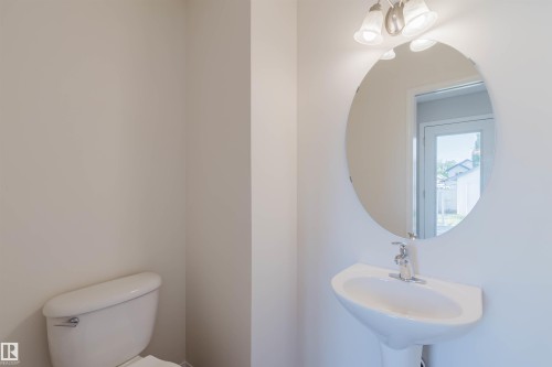 Pedestal sink with chrome faucet, oval mirror, and wall-mounted vanity lighting - 21332 89 Avenue Nw, Edmonton, AB - Indoor Photo Showing Bathroom
