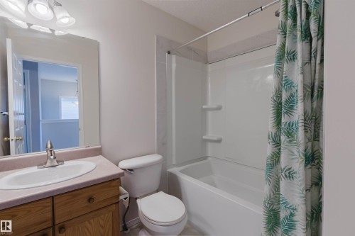 Full bathroom featuring a single vanity with wood cabinetry, a built-in mirror, an integrated sink, a commode, and a tub-shower combination - 21332 89 Avenue Nw, Edmonton, AB - Indoor Photo Showing Bathroom