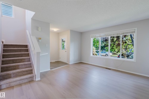 Expansive main living area featuring light wood-finish flooring, a large window with white trim, and a prominent staircase with carpeted treads - 21332 89 Avenue Nw, Edmonton, AB - Indoor Photo Showing Other Room