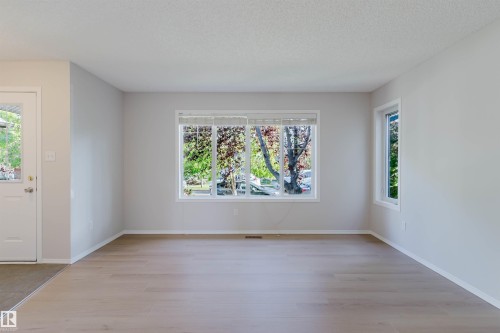 Spacious interior with light wood-finish flooring, multiple windows, and a white entry door with frosted glass - 21332 89 Avenue Nw, Edmonton, AB - Indoor Photo Showing Other Room