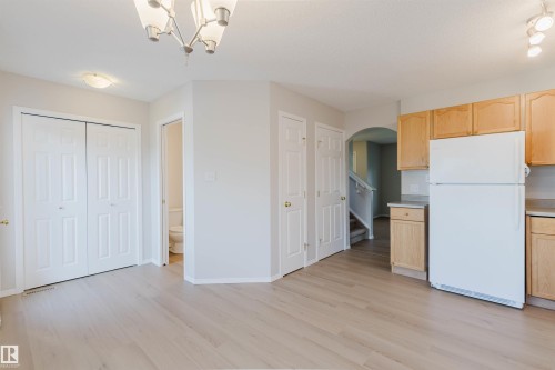 Wood-finish flooring, light tone wall paint, kitchen cabinetry with wood-finish doors, built-in refrigerator, and a chandelier with frosted glass shades - 21332 89 Avenue Nw, Edmonton, AB - Indoor Photo Showing Kitchen