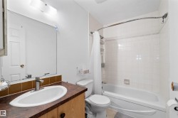 Integrated bathtub and shower with white subway tile surround, single vanity with oval sink, and mounted mirror with strip lighting - 
