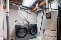 Laundry area with a water heater and exposed overhead utility lines - 