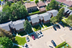 Multi-unit residential structure with dark shingle roofing, brick exterior, and landscaped grounds featuring mature trees and green spaces - 