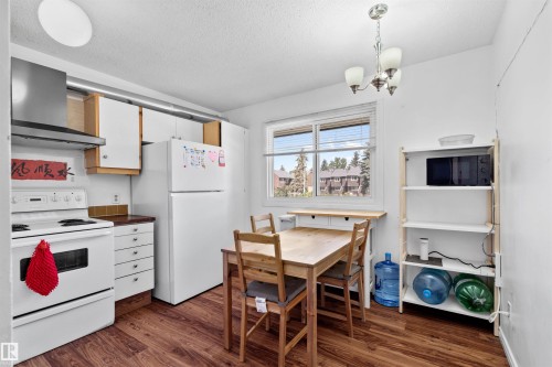 Kitchen featuring white appliances, upper and lower white cabinetry, a stainless steel range hood, and wood-finish flooring - 2730 105 Street Nw, Edmonton, AB - Indoor Photo Showing Kitchen