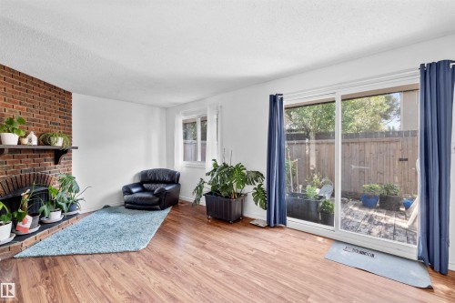 Brick-clad fireplace with mantel, wood-finish flooring, sliding glass door to outdoor space, and white walls - 2730 105 Street Nw, Edmonton, AB - Indoor Photo Showing Living Room With Fireplace
