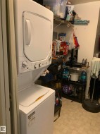 Stacked white washer and dryer unit, wire shelving, and light-toned flooring - 