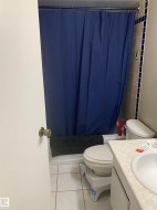 Bathroom featuring a built-in tub with a shower fixture, tile surround, white toilet, and a vanity with an integrated sink - 