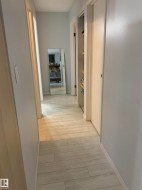Light-colored wood-finish tile flooring throughout, featuring a series of white paneled doors and light gray walls - 