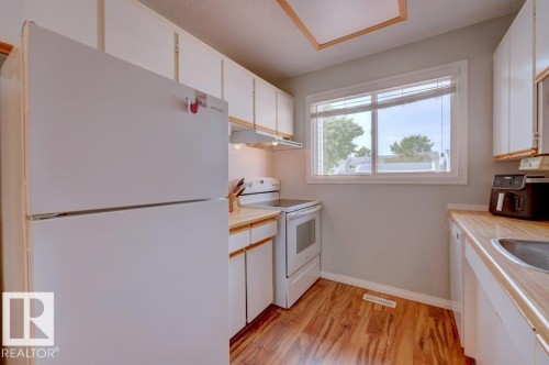 Kitchen featuring wood-finish flooring, white cabinetry, a built-in white refrigerator, a white electric range, and a stainless steel sink - 307 Northgate Terrace Nw, Edmonton, AB - Indoor Photo Showing Kitchen