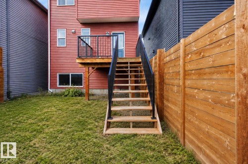 Backyard featuring a wood privacy fence, composite wood deck, wood stairs with metal railings, and a red siding exterior - 2355 Kelly Circle Circle Sw, Edmonton, AB - Outdoor With Exterior