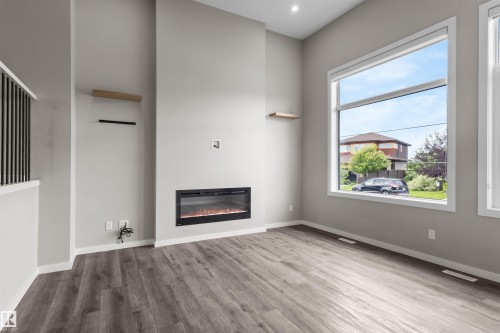 Spacious room featuring high ceilings, wood-finish flooring, a built-in electric fireplace, and large picture windows - 2355 Kelly Circle Circle Sw, Edmonton, AB - Indoor Photo Showing Other Room With Fireplace