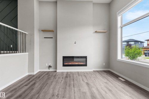 Spacious room featuring wood-finish flooring, an electric fireplace, a large window, and light-colored walls - 2355 Kelly Circle Circle Sw, Edmonton, AB - Indoor With Fireplace