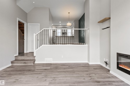 Wood-finish flooring, an in-wall fireplace, a contemporary pendant light fixture, and a black metal staircase railing - 2355 Kelly Circle Circle Sw, Edmonton, AB - Indoor Photo Showing Other Room With Fireplace