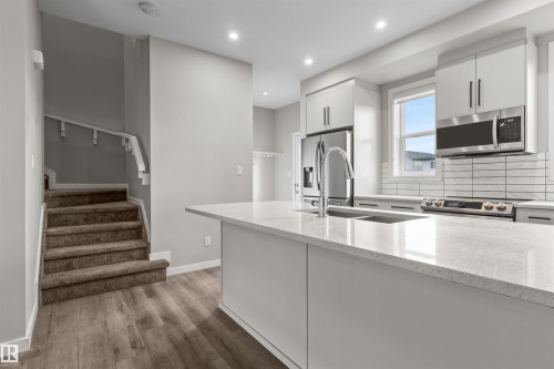 Modern kitchen featuring an island with a double basin sink, stainless steel appliances, white cabinetry, and a subway tile backsplash - 2355 Kelly Circle Circle Sw, Edmonton, AB - Indoor Photo Showing Kitchen With Double Sink With Upgraded Kitchen
