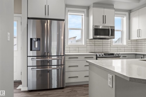Modern kitchen featuring stainless steel appliances, light-toned cabinetry, a subway tile backsplash, light-hued countertops, and wood-finish flooring - 2355 Kelly Circle Circle Sw, Edmonton, AB - Indoor Photo Showing Kitchen With Stainless Steel Kitchen With Upgraded Kitchen
