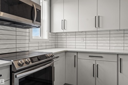 Stainless steel over-the-range microwave, electric range with a smooth cooktop, light grey flat-panel cabinetry with matte black hardware, white subway tile backsplash, and light-toned countertops - 2355 Kelly Circle Circle Sw, Edmonton, AB - Indoor Photo Showing Kitchen
