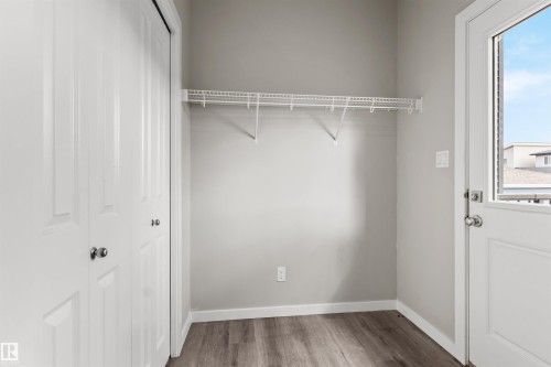 Wood-finish flooring, white bi-fold closet doors with polished hardware, white wire shelving unit, and a white exterior door with glass panel - 2355 Kelly Circle Circle Sw, Edmonton, AB - Indoor