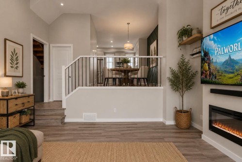 High ceilings with recessed lighting, wood-finish flooring, half-wall with iron balusters, and an electric fireplace with a wall-mounted display - 2355 Kelly Circle Circle Sw, Edmonton, AB - Indoor With Fireplace