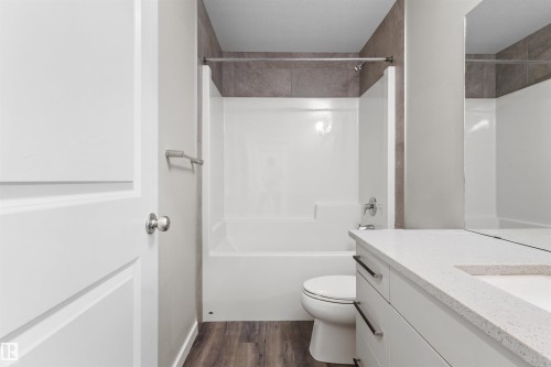 White paneled door, wood-finish flooring, white vanity with stone-finish countertop, integrated rectangular sink, and chrome fixtures - 2355 Kelly Circle Circle Sw, Edmonton, AB - Indoor Photo Showing Bathroom