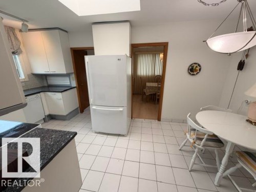 Bright kitchen with white cabinetry, dark speckled countertops, and a white tile floor - 6824 89 Avenue Nw, Edmonton, AB - Indoor
