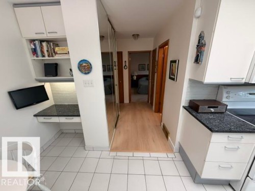 Kitchen and hallway featuring white cabinetry, dark stone-finish countertops, tile flooring, light wood-finish flooring, and mirrored closet doors - 6824 89 Avenue Nw, Edmonton, AB - Indoor Photo Showing Other Room