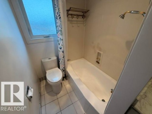 Bathroom featuring a white porcelain toilet, white square floor tiles, a privacy window, and a bathtub with a shower fixture - 6824 89 Avenue Nw, Edmonton, AB - Indoor Photo Showing Bathroom