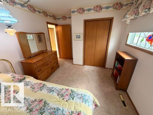 Carpeted interior with wood-finish bi-fold closet doors and a stained glass window feature - 6824 89 Avenue Nw, Edmonton, AB - Indoor Photo Showing Bedroom