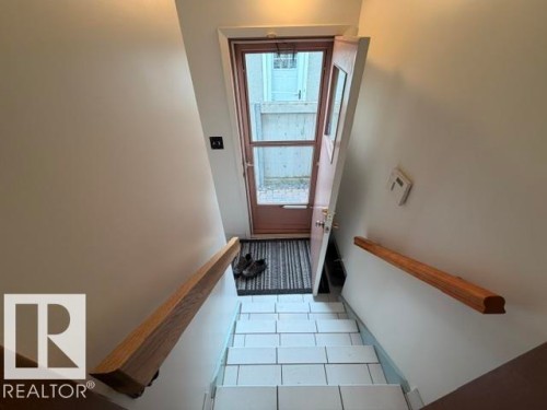 Entryway featuring a wood-panel door with glass inserts, a striped floor mat, white tiled stairs, and natural wood handrails - 6824 89 Avenue Nw, Edmonton, AB - Indoor Photo Showing Other Room