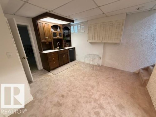 Built-in wet bar featuring wood cabinetry, integrated sink with faucet, white countertop, and under-cabinet lighting - 6824 89 Avenue Nw, Edmonton, AB - Indoor
