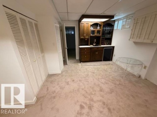 Lower-level recreational space featuring a built-in wet bar with wood cabinetry, a sink, and integrated shelving - 6824 89 Avenue Nw, Edmonton, AB - Indoor