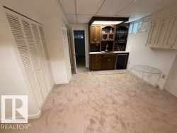 Lower-level recreational space featuring a built-in wet bar with wood cabinetry, a sink, and integrated shelving - 