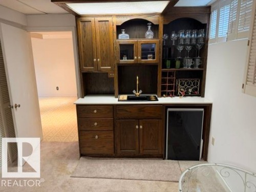 Built-in wood-finish wet bar featuring integrated shelving, cabinetry, a sink with a gold-tone faucet, and an under-counter beverage refrigerator - 6824 89 Avenue Nw, Edmonton, AB - Indoor