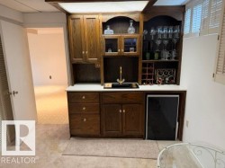 Built-in wood-finish wet bar featuring integrated shelving, cabinetry, a sink with a gold-tone faucet, and an under-counter beverage refrigerator - 