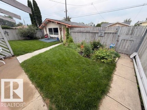 Expansive backyard featuring a manicured lawn, established garden beds, and a concrete pathway - 6824 89 Avenue Nw, Edmonton, AB - Outdoor
