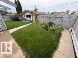 Expansive backyard featuring a manicured lawn, established garden beds, and a concrete pathway - 