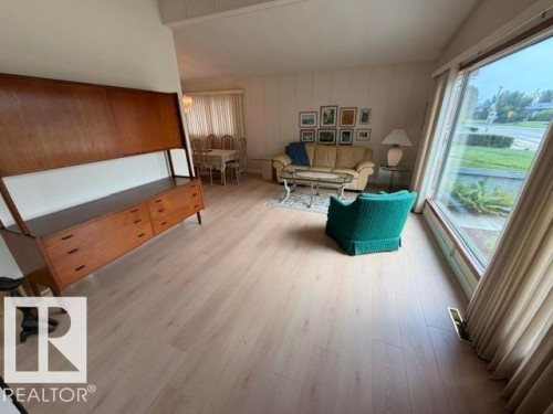 Spacious living area featuring light wood-finish flooring, a large picture window, and a built-in wood divider - 6824 89 Avenue Nw, Edmonton, AB - Indoor