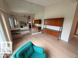 Living area featuring light wood-finish flooring, a full mirrored wall, and white baseboards - 